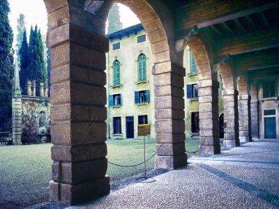 A view through a stone arcade with rusticated columns looking out onto a gravel courtyard and a yellow building with green shutters, identified by the filename as the courtyard and portico of Palazzo Giusti.