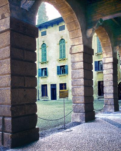 A view through a stone arcade with rusticated columns looking out onto a gravel courtyard and a yellow building with green shutters, identified by the filename as the courtyard and portico of Palazzo Giusti.
