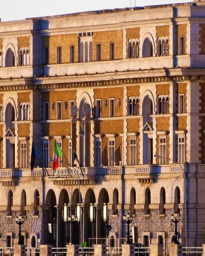 A large, ornate historic building with arched windows and a stone facade, featuring Italian and regional flags and the word "PROVINCIA" inscribed above the entrance.