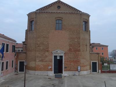 A large, cylindrical brick church with a triangular pediment and central entrance, viewed from a stone staircase leading up to a paved square, with adjacent buildings and a cloudy sky.