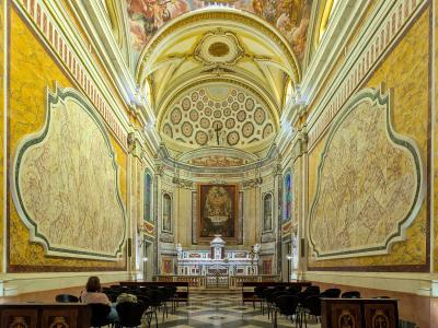 The interior of a church featuring yellow marble walls, a vaulted ceiling with frescoes, and an altar at the far end.