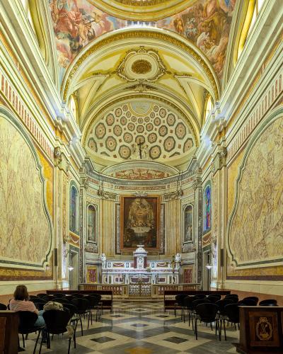 The interior of a church featuring yellow marble walls, a vaulted ceiling with frescoes, and an altar at the far end.