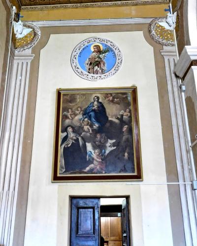 Interior wall of a church featuring a large framed painting of religious figures, a circular medallion with an image of Saint Blase (San Biagio) above it, and fluted pilasters.