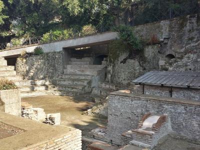 The image shows ancient Roman archaeological ruins featuring tiered brick seating, stone foundations, and a modern concrete walkway overhead, with no visible signage or specific identifying text.