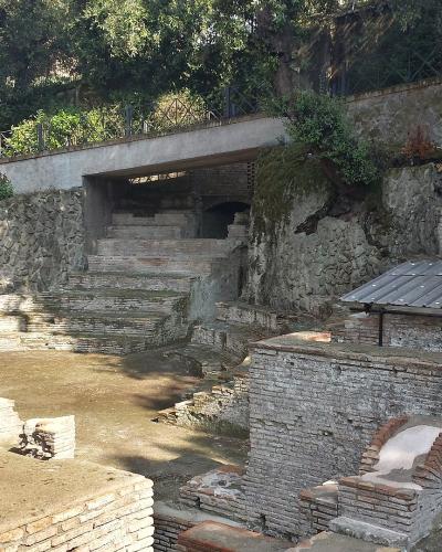 The image shows ancient Roman archaeological ruins featuring tiered brick seating, stone foundations, and a modern concrete walkway overhead, with no visible signage or specific identifying text.