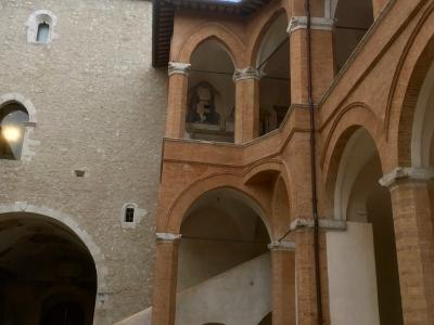 The image shows an interior courtyard of a historic fortress featuring a two-story brick loggia with pointed arches and a stone wall, with a person visible in the lower left corner.