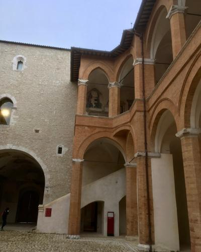 The image shows an interior courtyard of a historic fortress featuring a two-story brick loggia with pointed arches and a stone wall, with a person visible in the lower left corner.