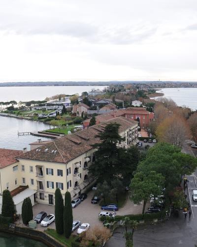 An elevated view of the Sirmione peninsula on Lake Garda, featuring the Hotel Terme di Sirmione in the foreground and the town extending into the lake with the distant shoreline visible.