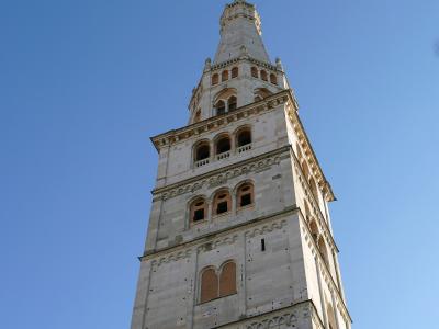 A low-angle photograph of a tall, ornate stone bell tower with multiple tiers of arched windows and decorative blind arcades, set against a clear blue sky.