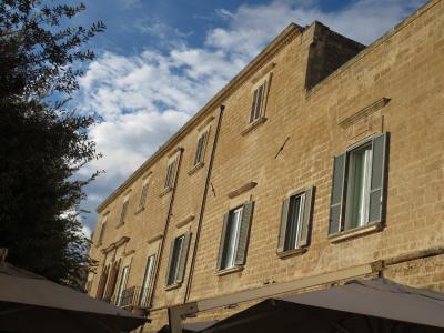 A low-angle shot of a large, light-colored stone building with shuttered windows and a tree on the left, taken from behind outdoor umbrellas under a blue sky.