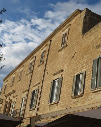 A low-angle shot of a large, light-colored stone building with shuttered windows and a tree on the left, taken from behind outdoor umbrellas under a blue sky.