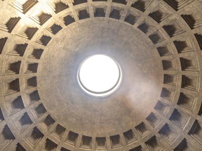 A low-angle photograph looking directly up into the coffered interior of a massive concrete dome, centered on the circular oculus opening to the sky.