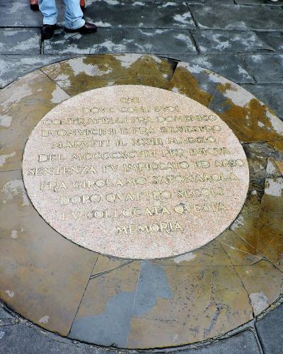 A circular stone memorial plaque embedded in a paved square, inscribed with Latin text commemorating the execution of Fra Girolamo Savonarola and his followers on May 23, 1498.