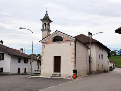The image shows a small, standalone church with a bell tower and a pedimented facade, situated at a street intersection in a residential area; the filename indicates the location is Sartena, Italy.