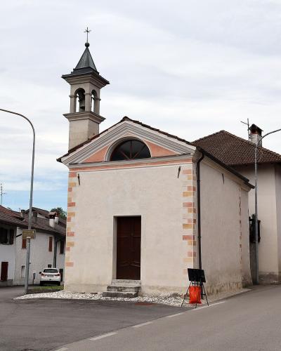 The image shows a small, standalone church with a bell tower and a pedimented facade, situated at a street intersection in a residential area; the filename indicates the location is Sartena, Italy.