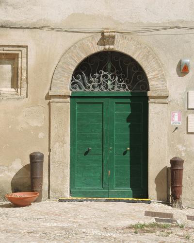 The image shows the entrance to a building with a green double door under an arched brick frame, flanked by two old cannons and a terracotta bowl, with stone plaques on the wall reading "MUSEO D'ARTE MODERNA 'MEDITERRANIA'" and "MUSEO DEL COSTUME"