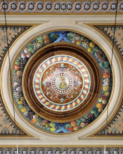 The image shows an ornate, painted ceiling medallion featuring a central portrait surrounded by fruit garlands and geometric patterns, with decorative borders and hanging wires visible.