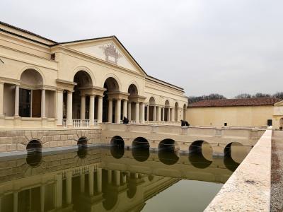 A Renaissance palace featuring a long loggia with arches and columns, situated next to a rectangular reflecting pool with arched openings in its retaining wall.