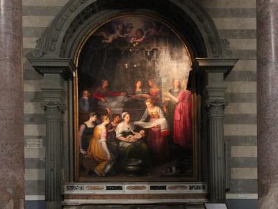 An interior view of a religious altar featuring a large painting of the Nativity of the Virgin Mary, framed by an arched stone structure and flanked by striped marble columns within a church.
