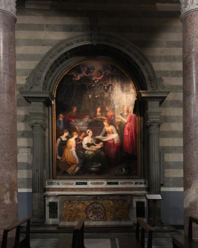 An interior view of a religious altar featuring a large painting of the Nativity of the Virgin Mary, framed by an arched stone structure and flanked by striped marble columns within a church.