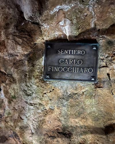 A close-up of a dark metal plaque mounted on a rough, textured limestone cave wall, inscribed with the text "SENTIERO CARLO FINOCCHIARO".
