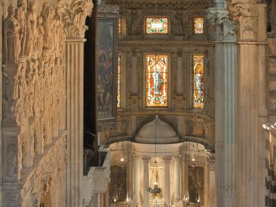 The image shows the ornate interior of a church, featuring a marble altar, stained glass windows, and a wall with numerous sculpted figures on the left.