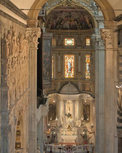 The image shows the ornate interior of a church, featuring a marble altar, stained glass windows, and a wall with numerous sculpted figures on the left.