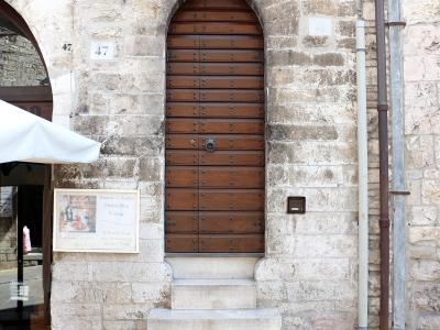 A close-up view of a tall, arched wooden door set into a weathered stone wall, with house numbers 47 and 49 visible, and a sign for "Fantasia di Crostini" to the left.