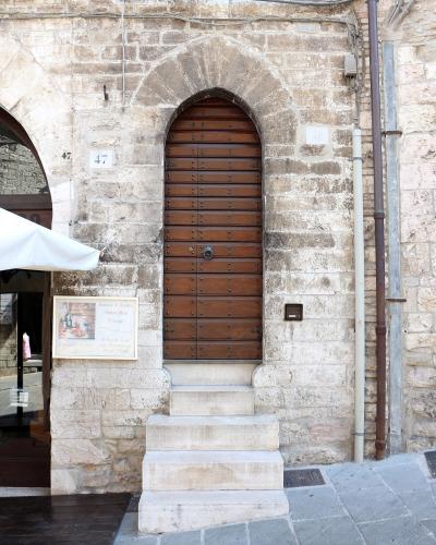 A close-up view of a tall, arched wooden door set into a weathered stone wall, with house numbers 47 and 49 visible, and a sign for "Fantasia di Crostini" to the left.