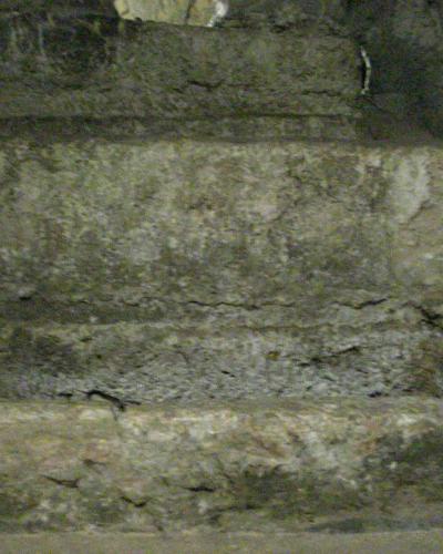 A close-up, low-light photograph of rough-hewn stone steps or a recessed stone niche within an underground tunnel, with no visible signage or distinct features.