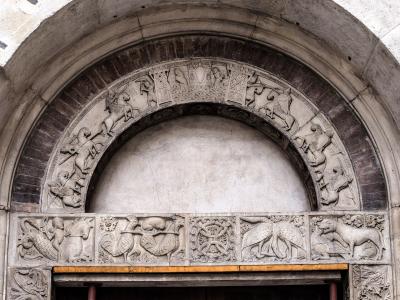A close-up photograph of a Romanesque stone portal featuring an archivolt with sculpted knights on horseback and a lintel with various animal and mythological carvings.