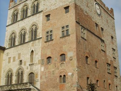 A tall, medieval-style stone and brick palace with crenellated battlements, arched windows, a clock face, and an external stone staircase leading to an upper entrance.