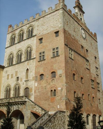 A tall, medieval-style stone and brick palace with crenellated battlements, arched windows, a clock face, and an external stone staircase leading to an upper entrance.