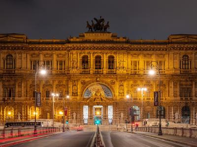 The image shows the Palazzo di Giustizia (Palace of Justice) in Rome, Italy, illuminated at night, with the inscription "CORTE DI CASSAZIONE" visible on the facade and a quadriga sculpture atop the central section.