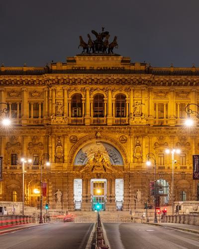 The image shows the Palazzo di Giustizia (Palace of Justice) in Rome, Italy, illuminated at night, with the inscription "CORTE DI CASSAZIONE" visible on the facade and a quadriga sculpture atop the central section.