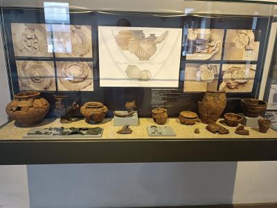 A museum display case containing various ancient pottery fragments and reconstructed vessels, with informational panels and diagrams behind them.