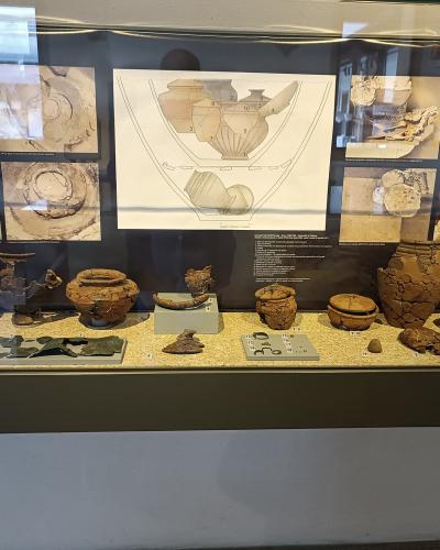 A museum display case containing various ancient pottery fragments and reconstructed vessels, with informational panels and diagrams behind them.