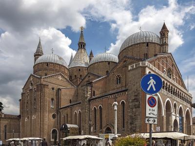 The image shows the exterior of a large brick basilica with multiple domes and spires, featuring a prominent blue pedestrian crossing sign and market stalls in the foreground under a cloudy sky.