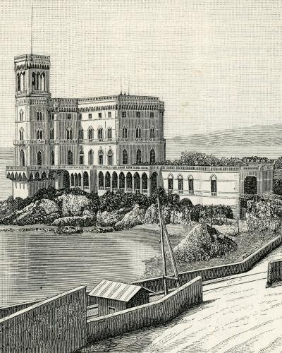 A vintage engraved illustration of a large, multi-story castle with a prominent square tower and arched windows, situated on a rocky promontory directly overlooking the sea, with a coastal road and small boat in the foreground.