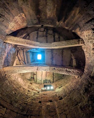 A view looking down into a deep, circular stone well with a spiral staircase winding down its walls and a bright opening at the top.