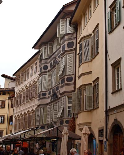 The image shows Piazza delle Erbe in Verona, Italy, featuring the Palazzo Maffei with its distinctive statues on the roofline, the Torre dei Lamberti to the left, and a central column with a statue (likely the Lion of Saint Mark) in the foreground
