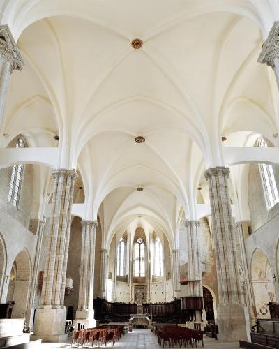 The interior of a large, light-colored stone church featuring tall clustered columns, ribbed vaulted ceilings, and rows of wooden pews facing an altar.