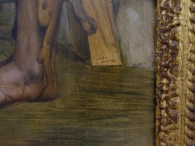 A close-up detail of a painted artwork showing a human foot and lower leg, with visible brushwork and a signature or inscription on a wooden element, framed by an ornate, gilded picture frame.