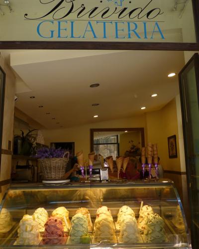 The image shows the storefront of "Brivido Gelateria," an ice cream shop with a display case of gelato, waffle cones, and interior lighting.
