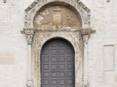 The image shows a close-up of an ornate, Gothic-style stone portal with a pointed arch, intricate carvings, and two sculpted lions at the base of the columns, set into a light-colored stone facade.
