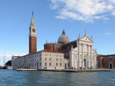 The image shows the Basilica of San Giorgio Maggiore, a white marble church with a prominent brick bell tower and a central dome, situated on an island in a body of water with boats visible nearby.