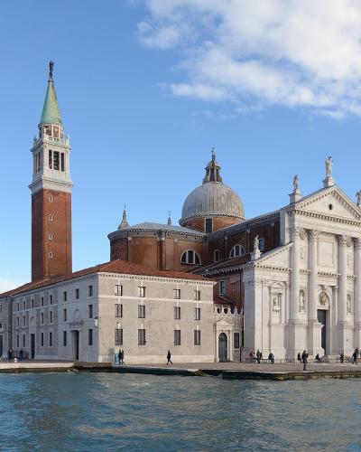 The image shows the Basilica of San Giorgio Maggiore, a white marble church with a prominent brick bell tower and a central dome, situated on an island in a body of water with boats visible nearby.
