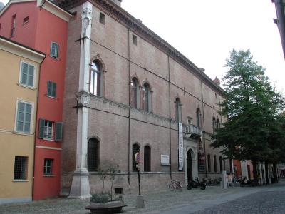 A large, historic brick building with arched windows and a prominent white stone buttress, identified by a vertical banner reading "Palazzo dei Principi" hanging near its entrance.