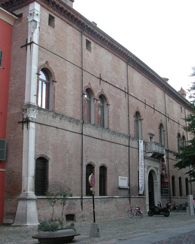 A large, historic brick building with arched windows and a prominent white stone buttress, identified by a vertical banner reading "Palazzo dei Principi" hanging near its entrance.