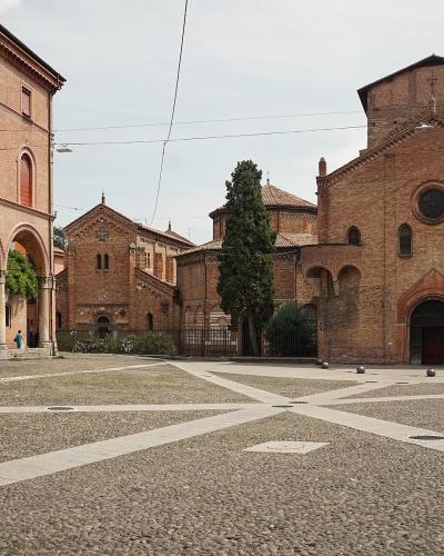 A view of Piazza Santo Stefano in Bologna, Italy, showing the distinctive brick architecture of the seven churches complex, including the Church of San Stefano Maggiore on the right and the arcaded buildings of the seminary on the left, with a cob